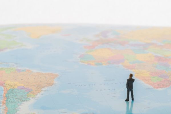 concept image of tiny businessman standing on world map, thinking about globalization