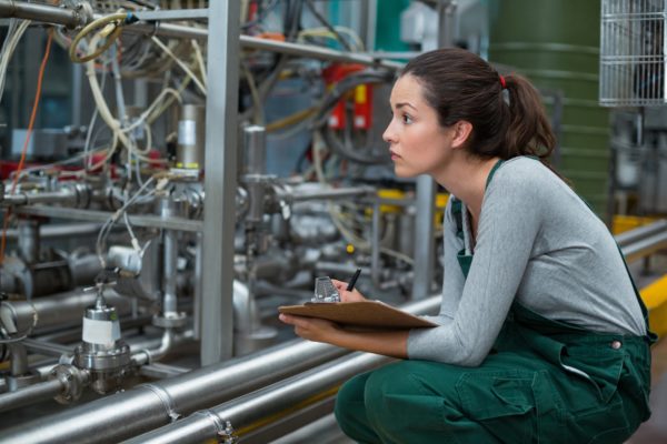 Product developer watching manufacturing process with clipboard in manufacturing facility